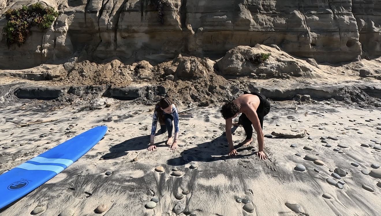 Carlsbad surf coach teaching a young student pop-up technique on the beach